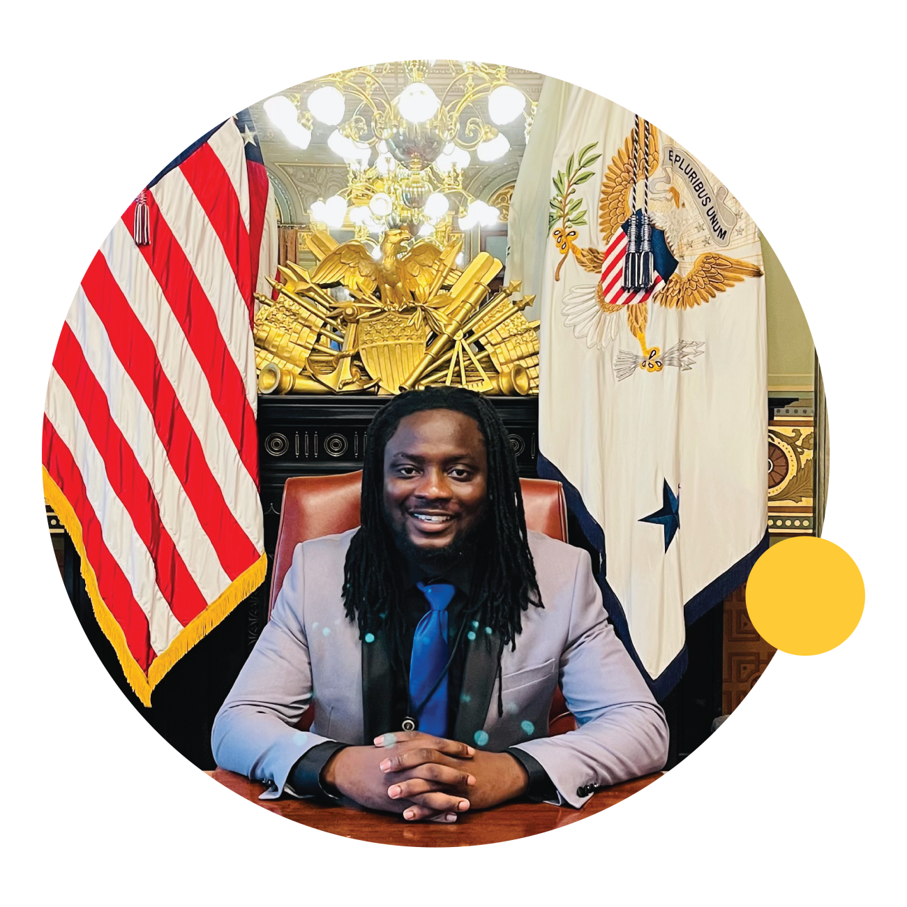 Prince Murray, a May 2021 ASU graduate, sits at a desk in front of the American flag.